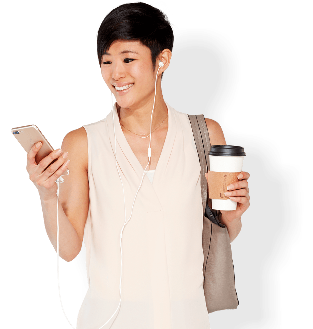 A young woman listening to headphones holds her mobile device in one hand, and a disposable coffee cup in the other